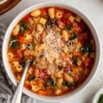Bowl of kale white bean minestrone soup with parmesan cheese on top and crusty bread on the side.