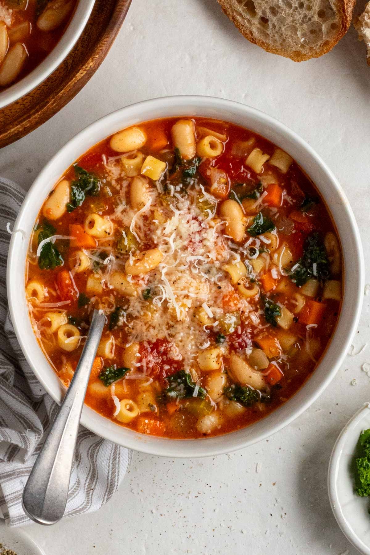 Bowl of kale white bean minestrone soup with parmesan cheese on top and crusty bread on the side.