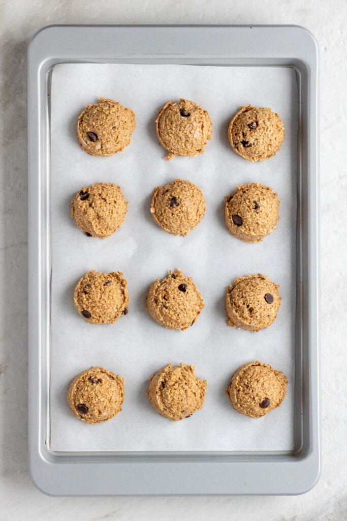 A large baking sheet lined with parchment with 12 scoops of banana bread bite batter.