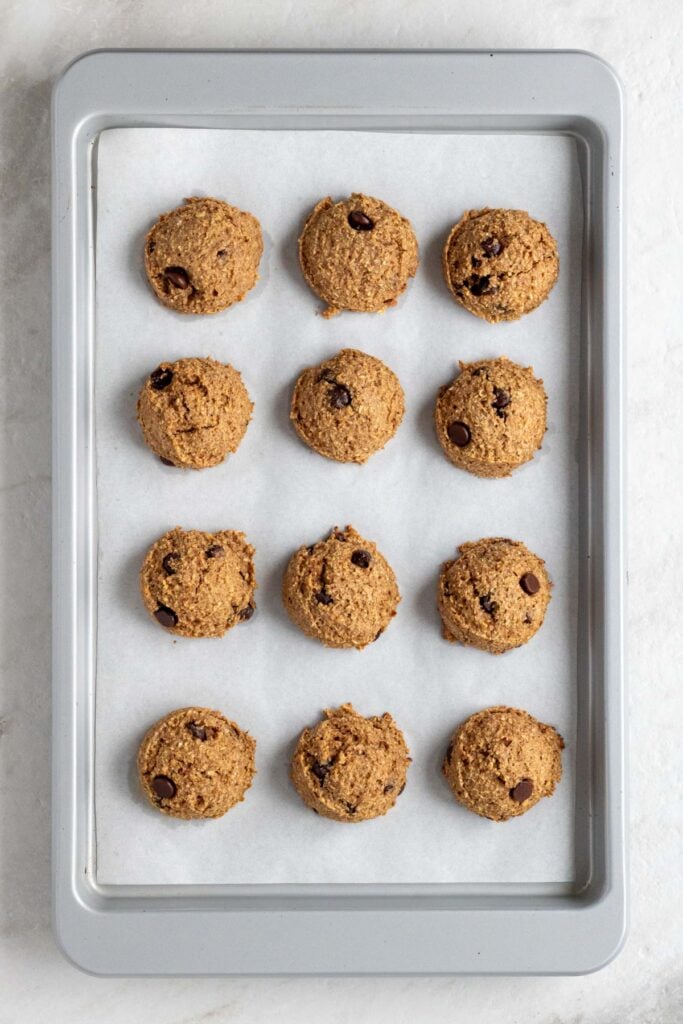 A large baking sheet lined with parchment with 12 cooked banana bread bites.