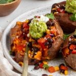 Close up of black been stuffed potatoes with a gold fork pressed into it with avocado and sour cream on top.