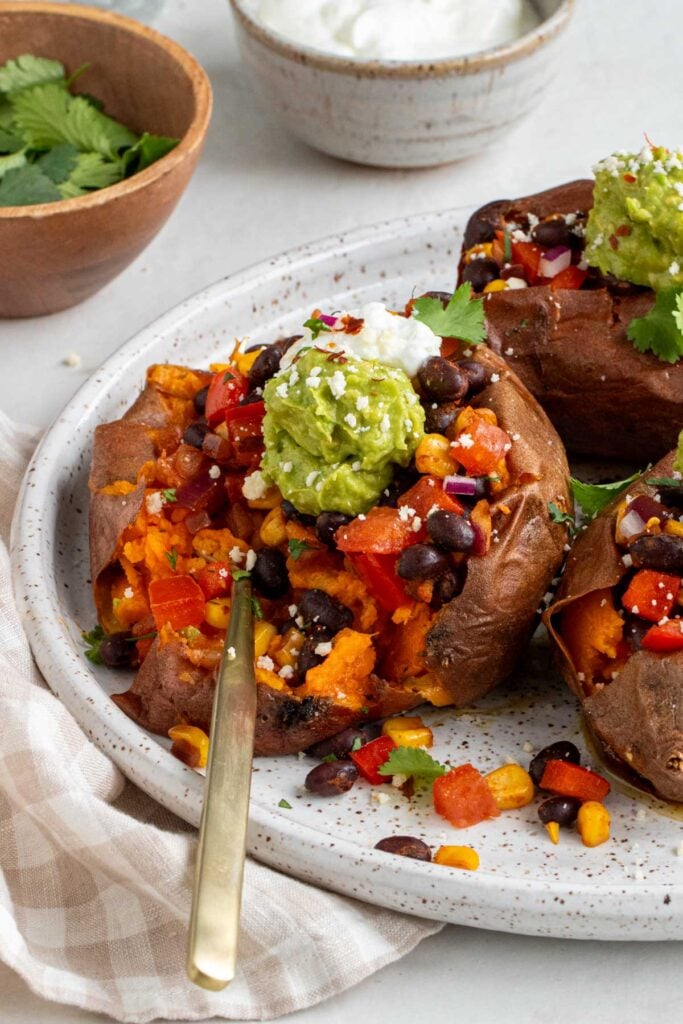 Close up of black been stuffed potatoes with a gold fork pressed into it with avocado and sour cream on top.