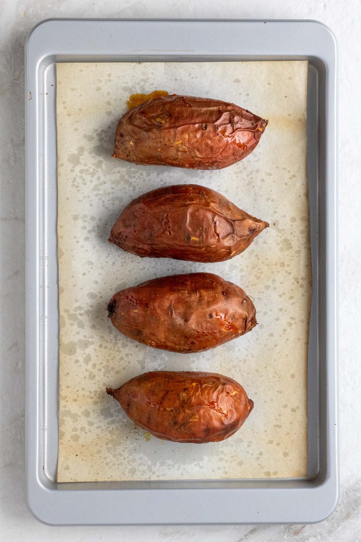 Baking sheet with parchment paper with four baked sweet potatoes on top.