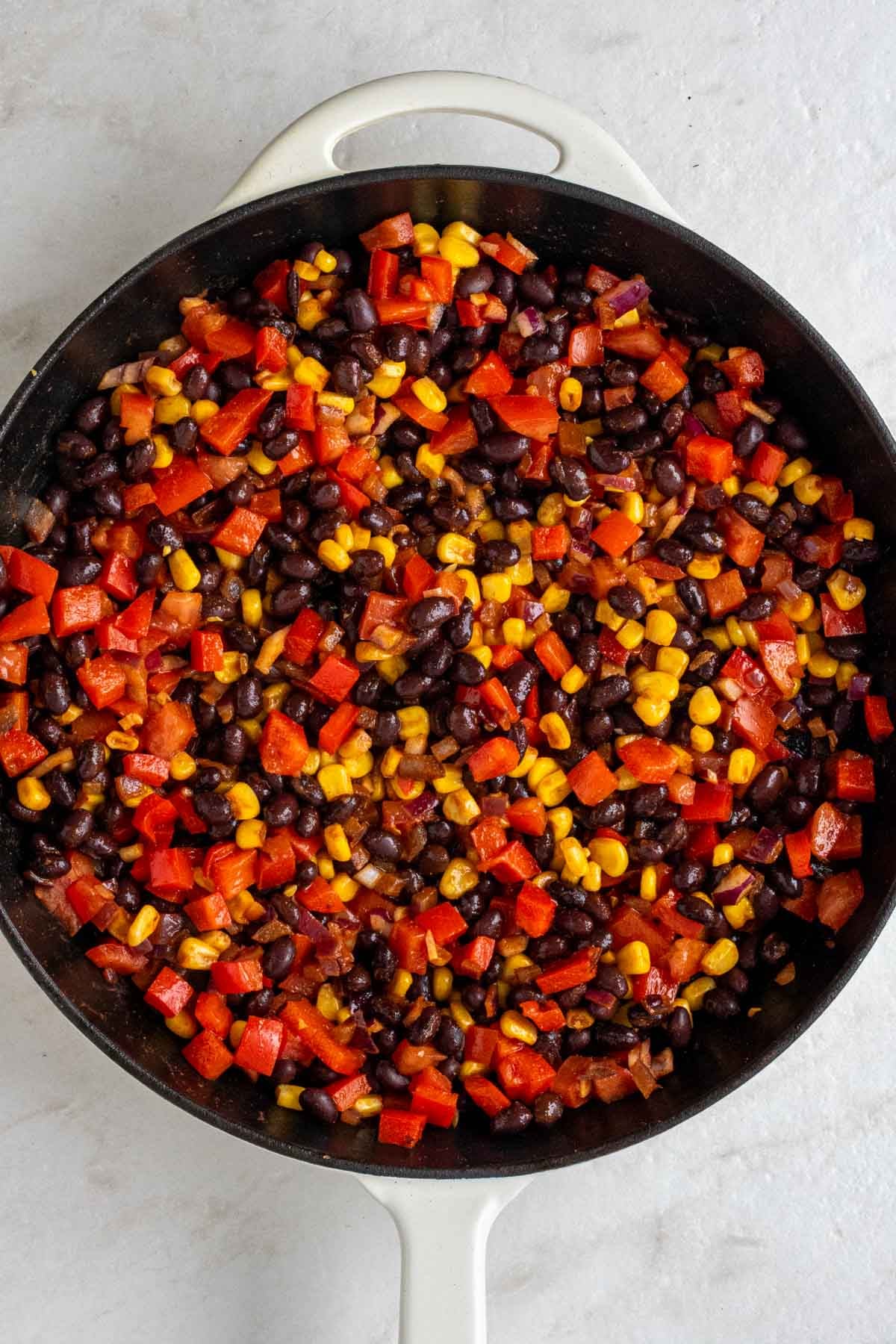 Cast-iron skillet with a spiced black bean mixture with red onion, red bell pepper, and corn.