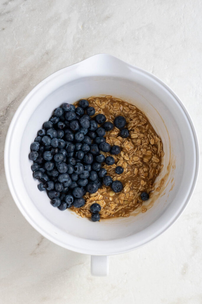 White mixing bowl of oat mixture with fresh blueberries on a white background.