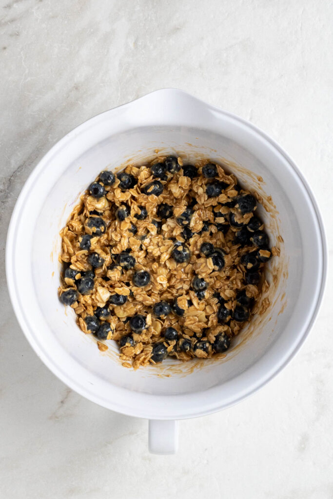 White mixing bowl with blueberry oatmeal batter on a white background.