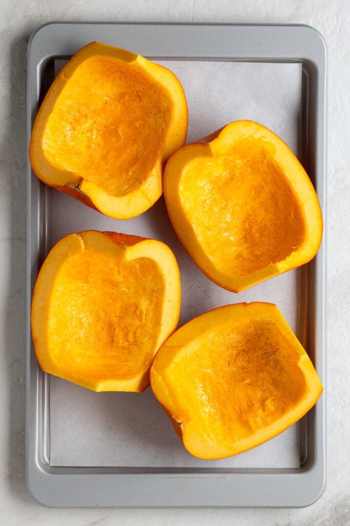 A raw pumpkin cut into quarters on a baking sheet with parchment paper.