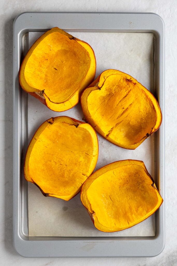 A roasted pumpkin cut into quarters on a baking sheet with parchment paper.