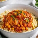 Bowl of slow cooker moroccan chicken served over couscous with fresh cilantro and fresh mint on top with a fork on a white background.