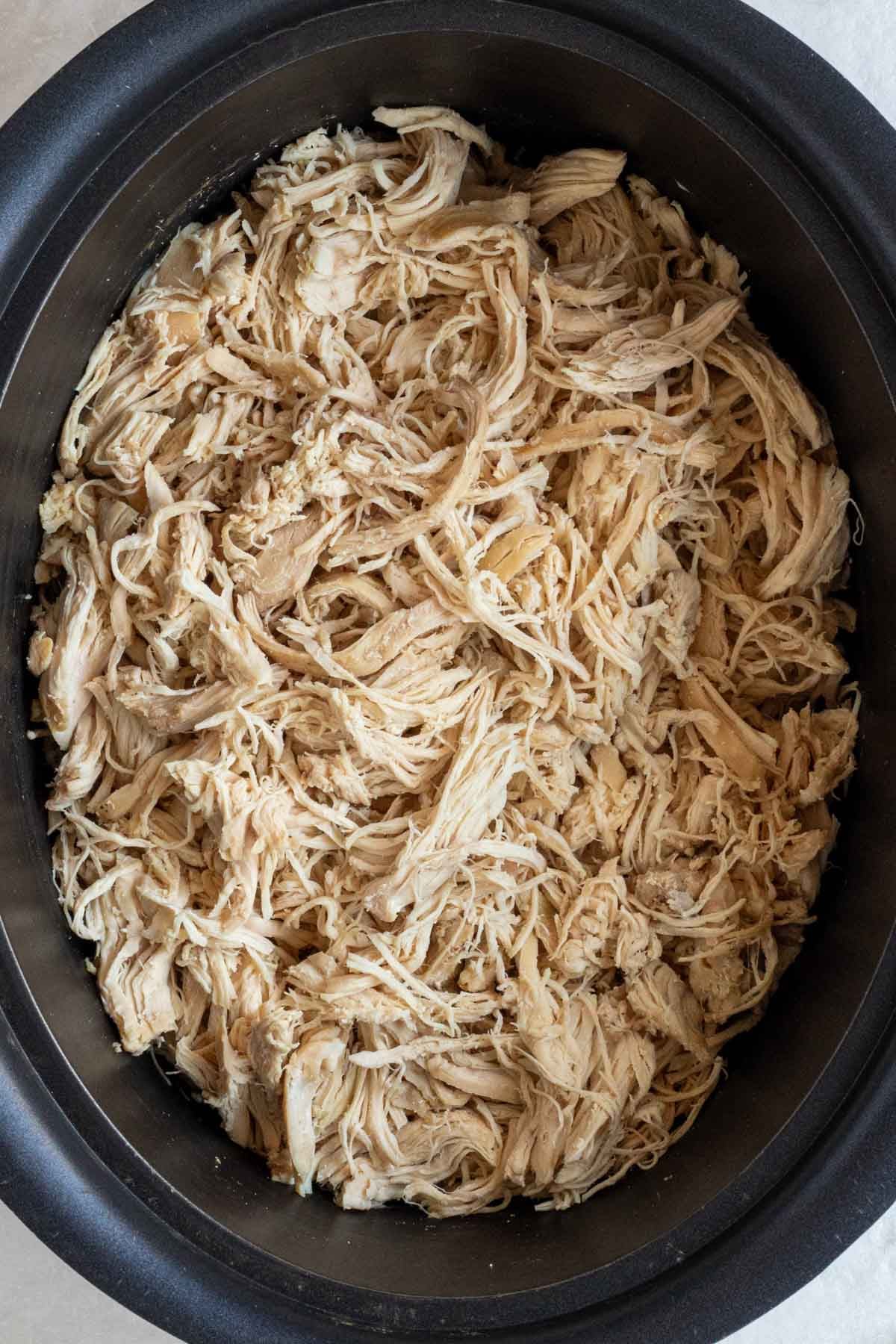 Close up of a crock pot filled with shredded chicken.
