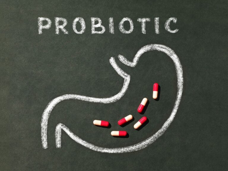 Chalkboard with a stomach drawn in chalk with probiotic capsule supplements on top.