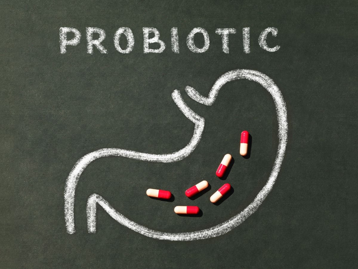 Chalkboard with a stomach drawn in chalk with probiotic capsule supplements on top.