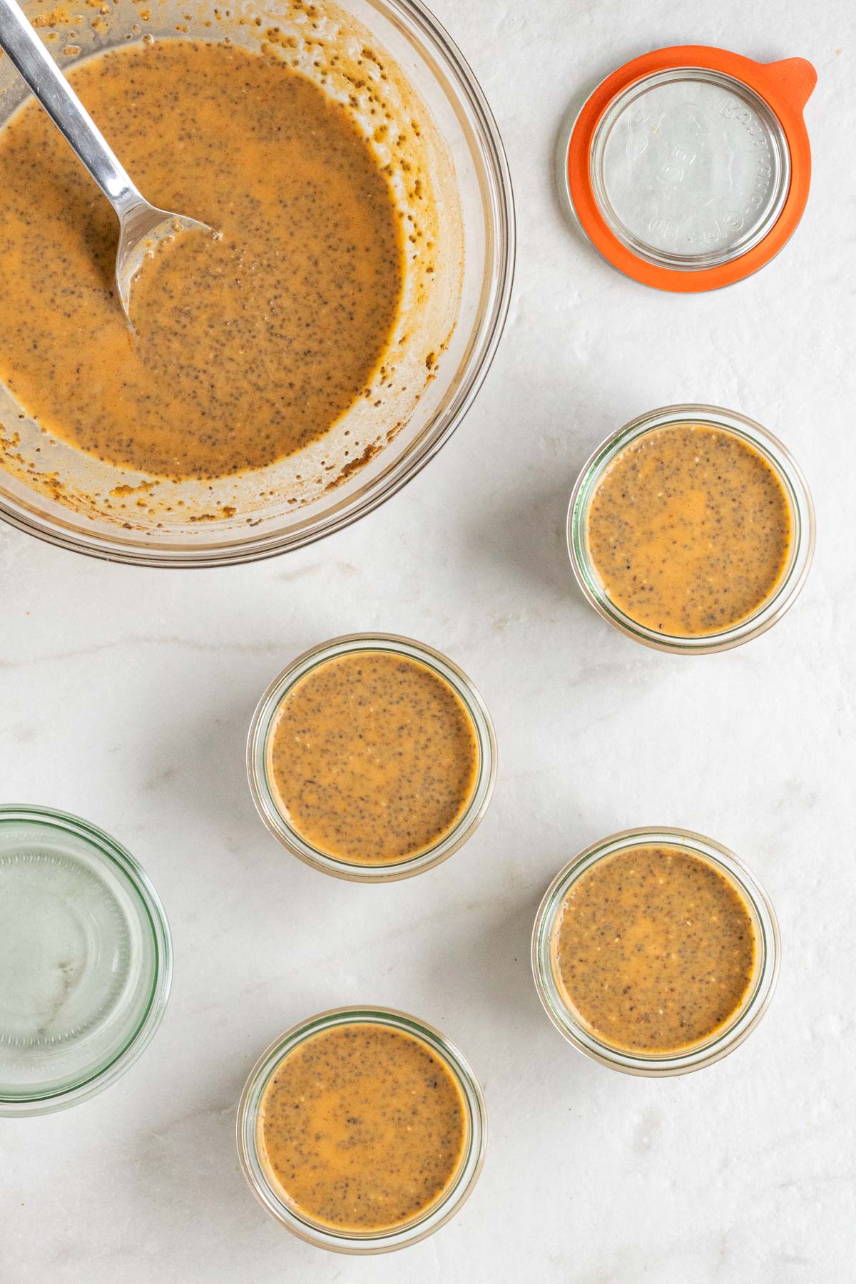 A glass bowl with pumpkin chia mixture with a silver serving spoon with four small glass jars filled with pumpkin chia mixture.