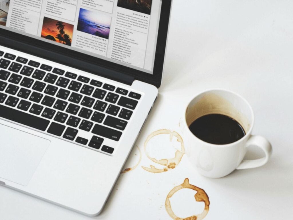 Laptop and cup of black coffee on a white background with coffee stains on the surface.