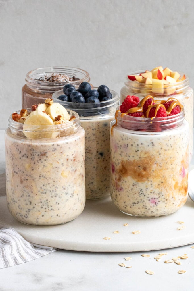 Five jars of different flavors of overnight oats on a white background.