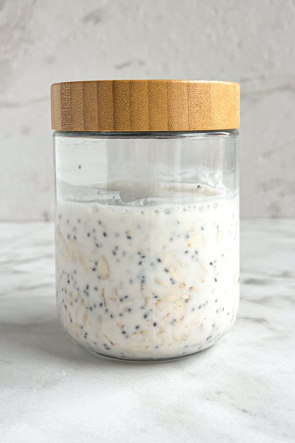 Jar of overnight oats with a wood lid on a white background.