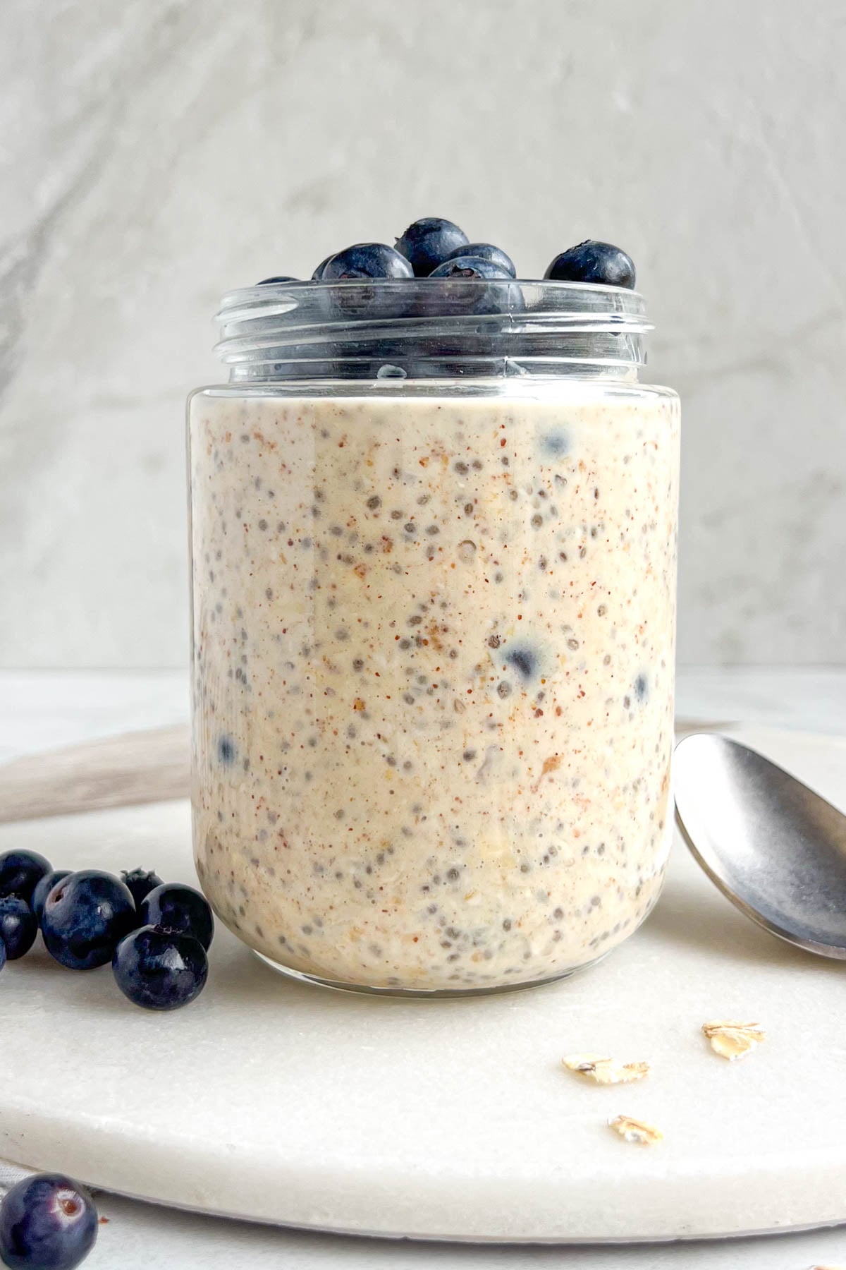 Jar of blueberry almond overnight oats on a white background with a spoon, rolled oats, and fresh blueberries on the side.