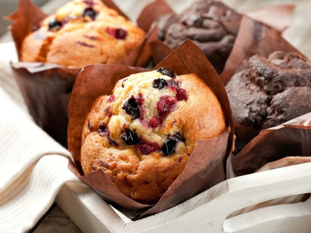 Bakery-style mixed berry muffins and double chocolate muffins in a wood basket with a tea towel.
