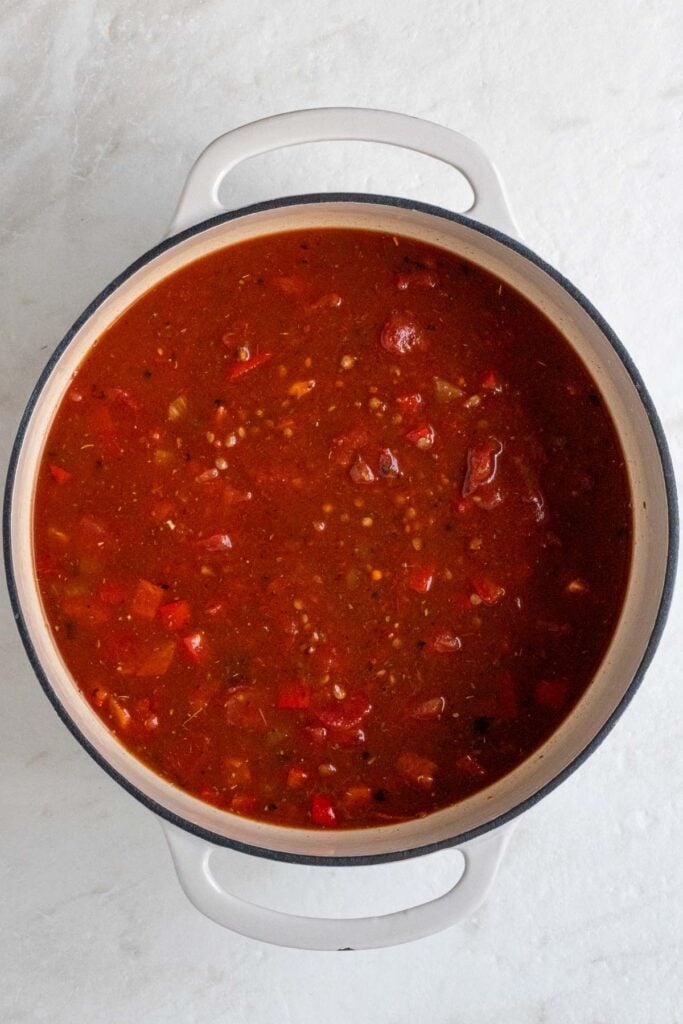 Pot with sautéed veggies, spices, lentils and tomato sauce on a white background.