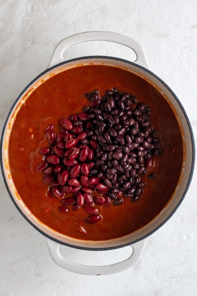 Pot with sautéed veggies, spices, lentils, tomato sauce with red kidney beans and black beans on a white background.