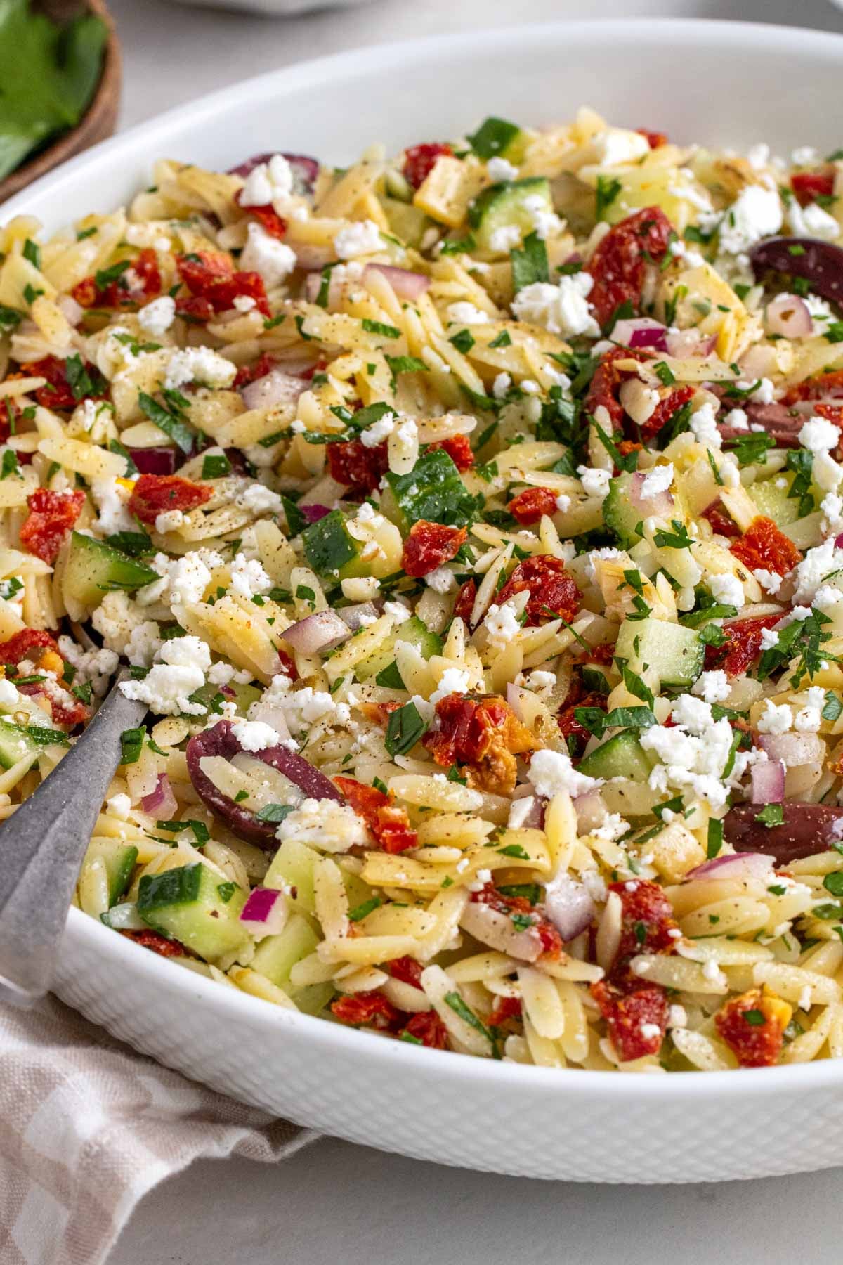 Close up of a large white bowl filled with Greek orzo pasta salad with a spoon.