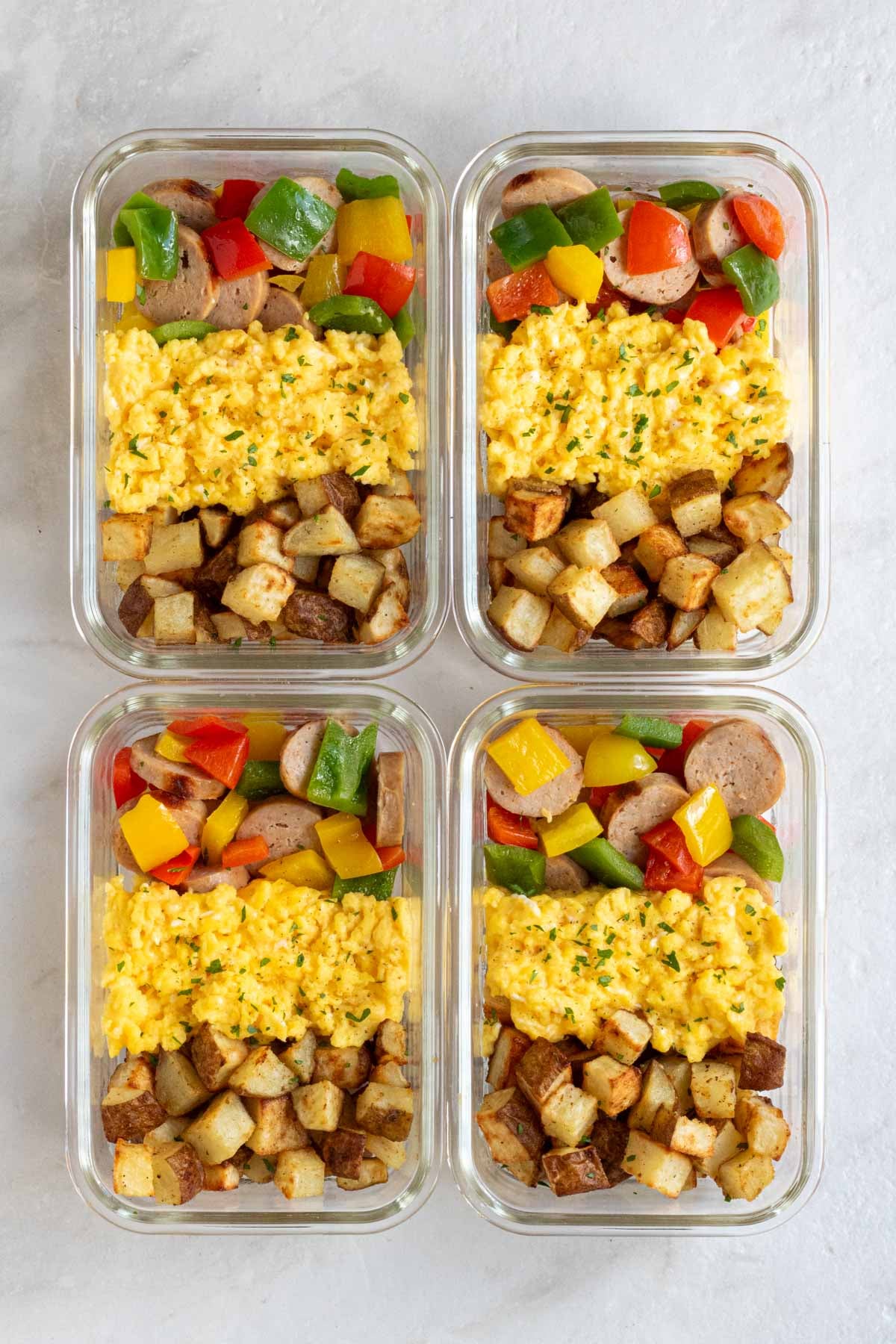 Four healthy meal prep breakfast bowls in glass containers on a white background.