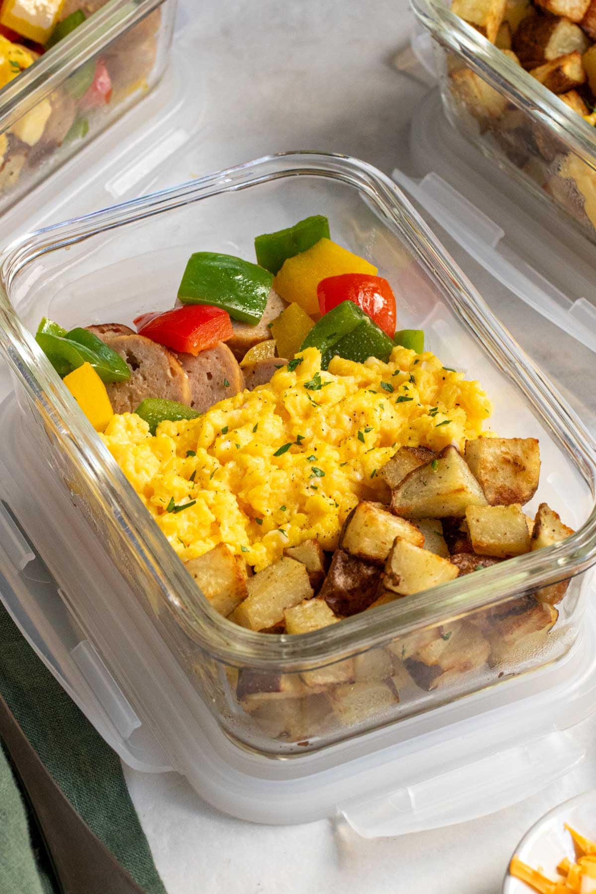 Close up of a meal prep container with breakfast potatoes, scrambled eggs, turkey sausage, and bell peppers.