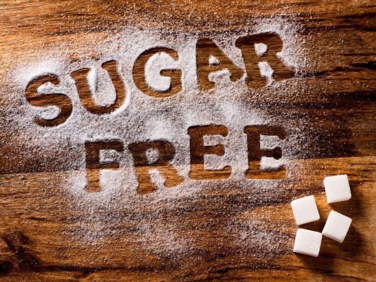 Sugar cubes and white sugar on a wood background with the words sugar free written into it.