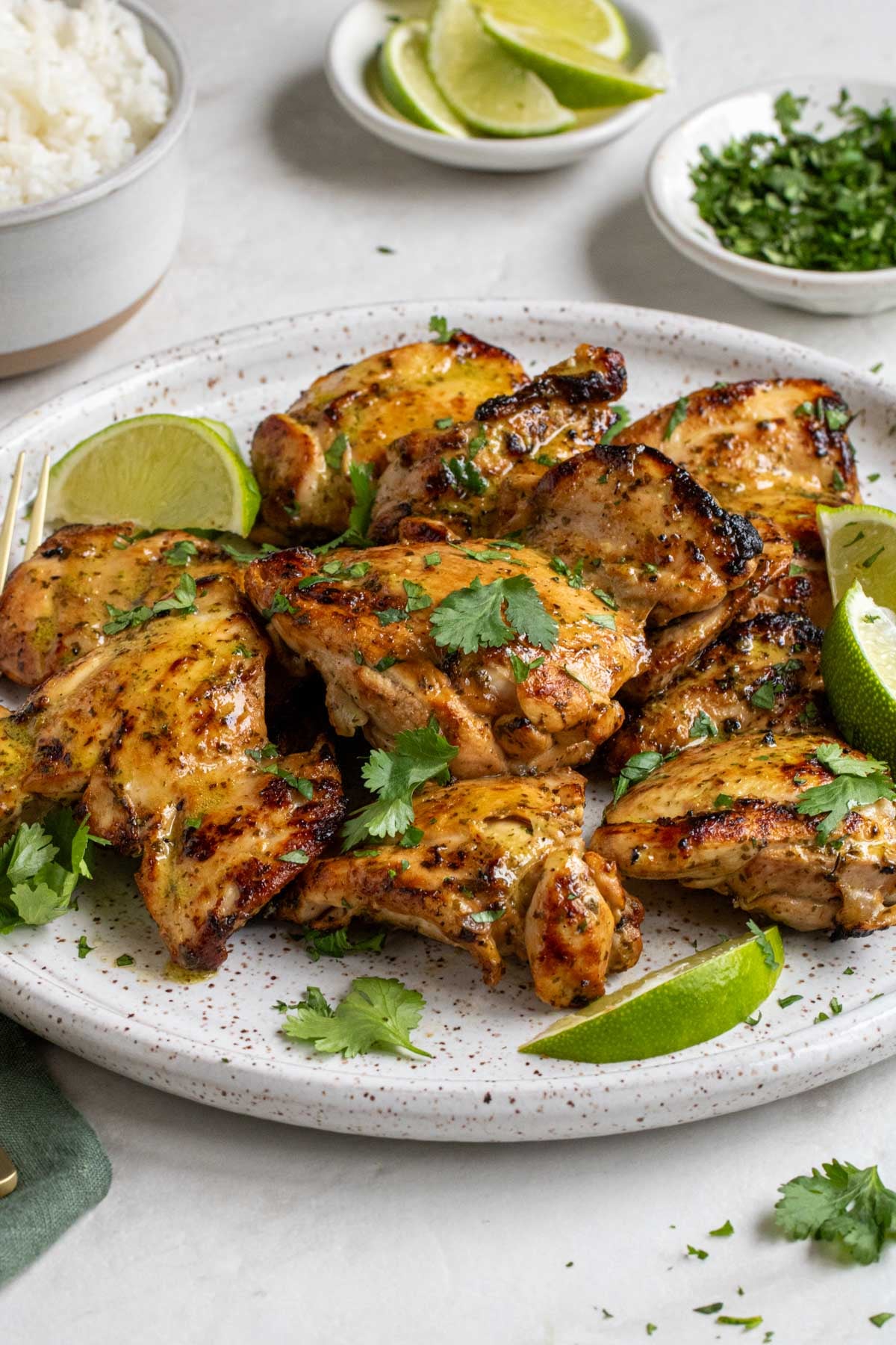 Close up of a plate of grilled cilantro lime chicken on a plate with lime wedges and fresh cilantro on top and a gold fork on the side.