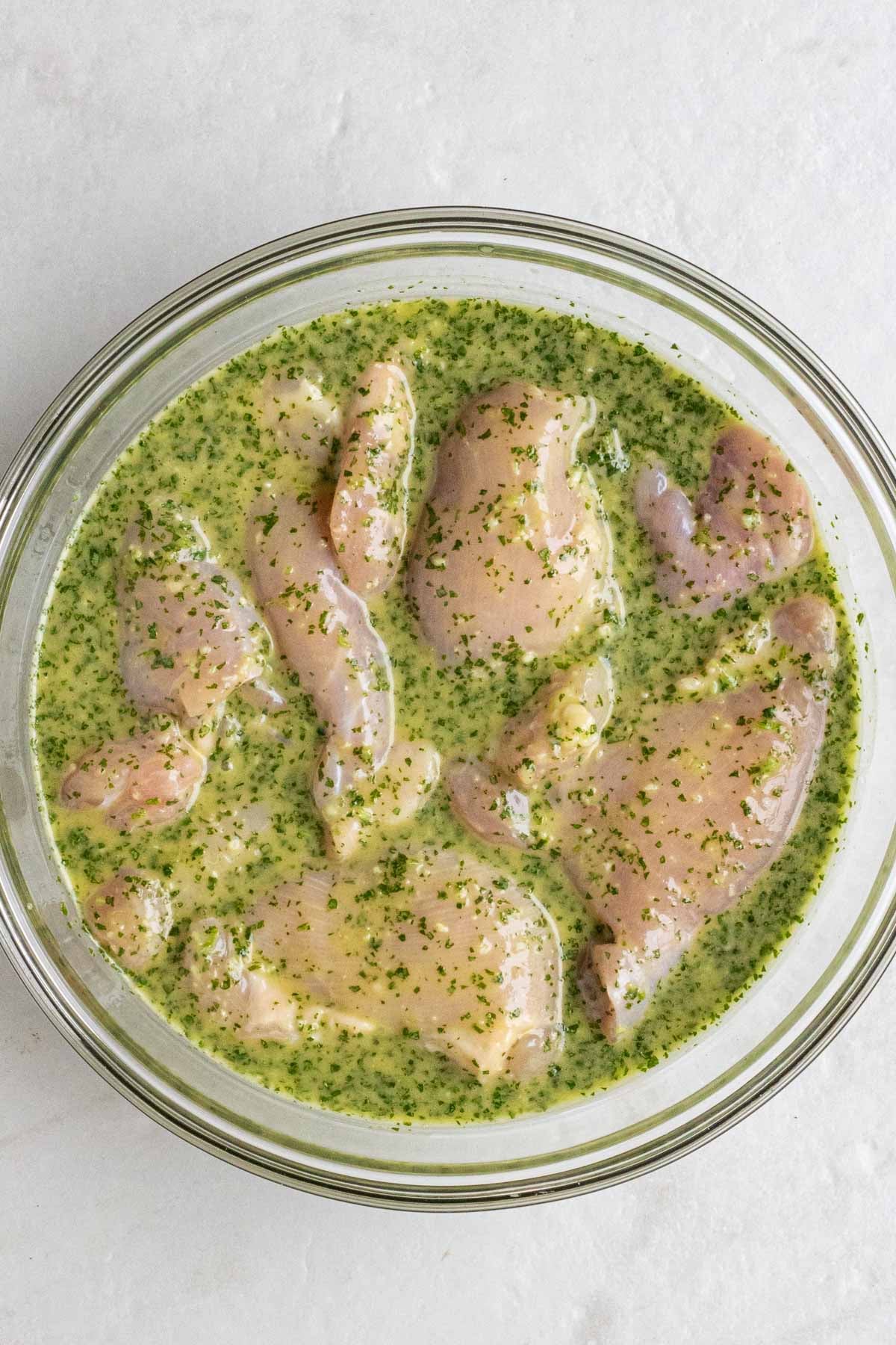 Large glass bowl of chicken thighs in cilantro lime marinade.