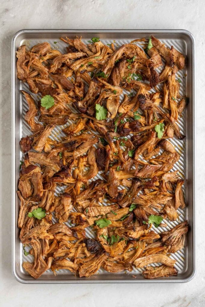 Large baking sheet with crispy pulled pork and fresh cilantro on top.
