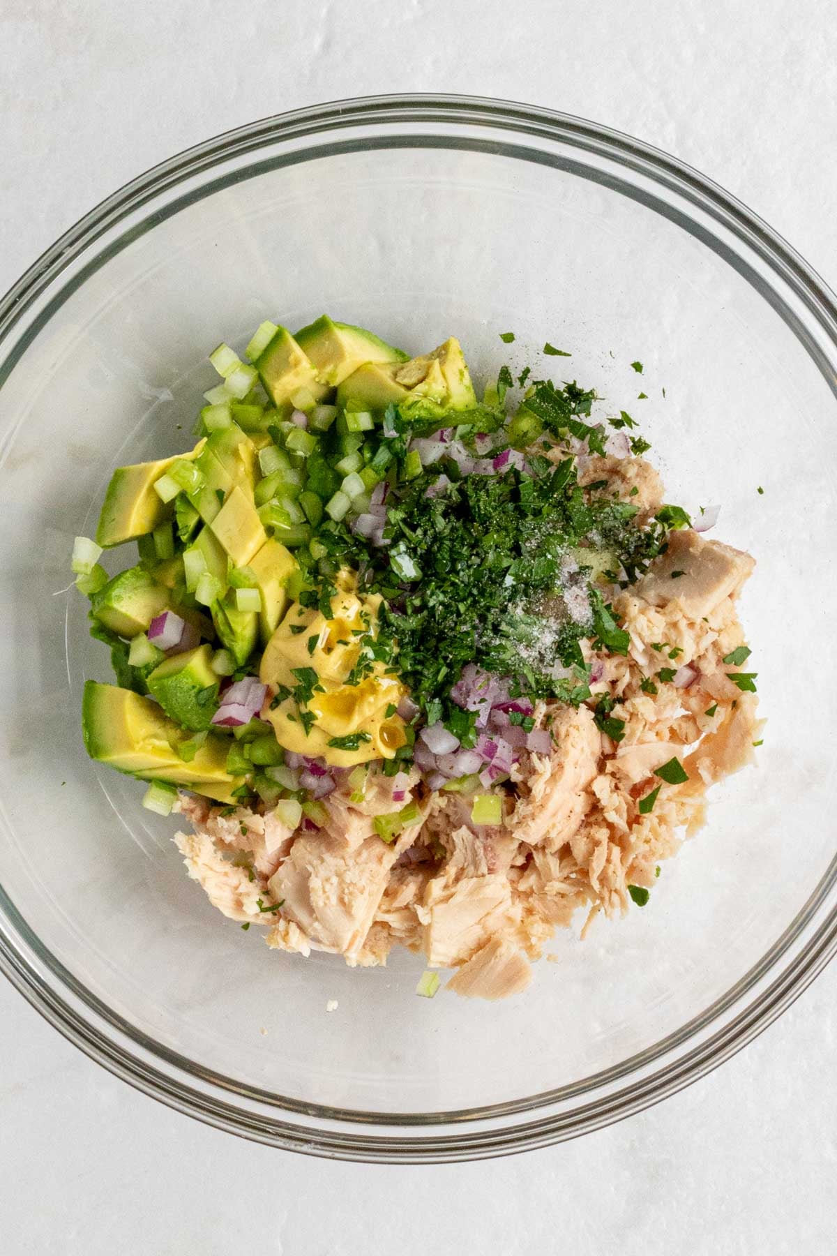 Glass bowl with flaked tuna, diced avocado, diced red onion, diced celery, Dijon mustard, olive oil, parsley, salt and pepper.