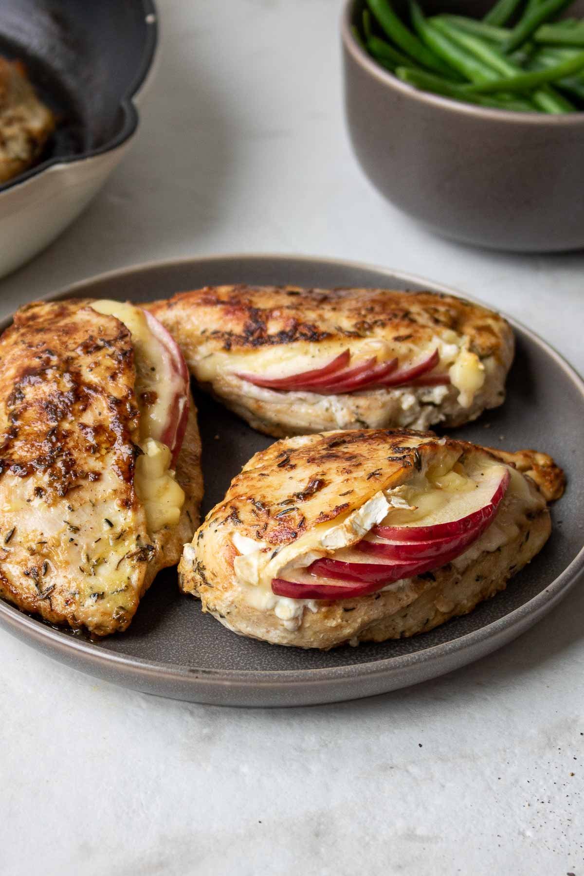 Cooked apple brie stuffed chicken breasts on a grey plate.