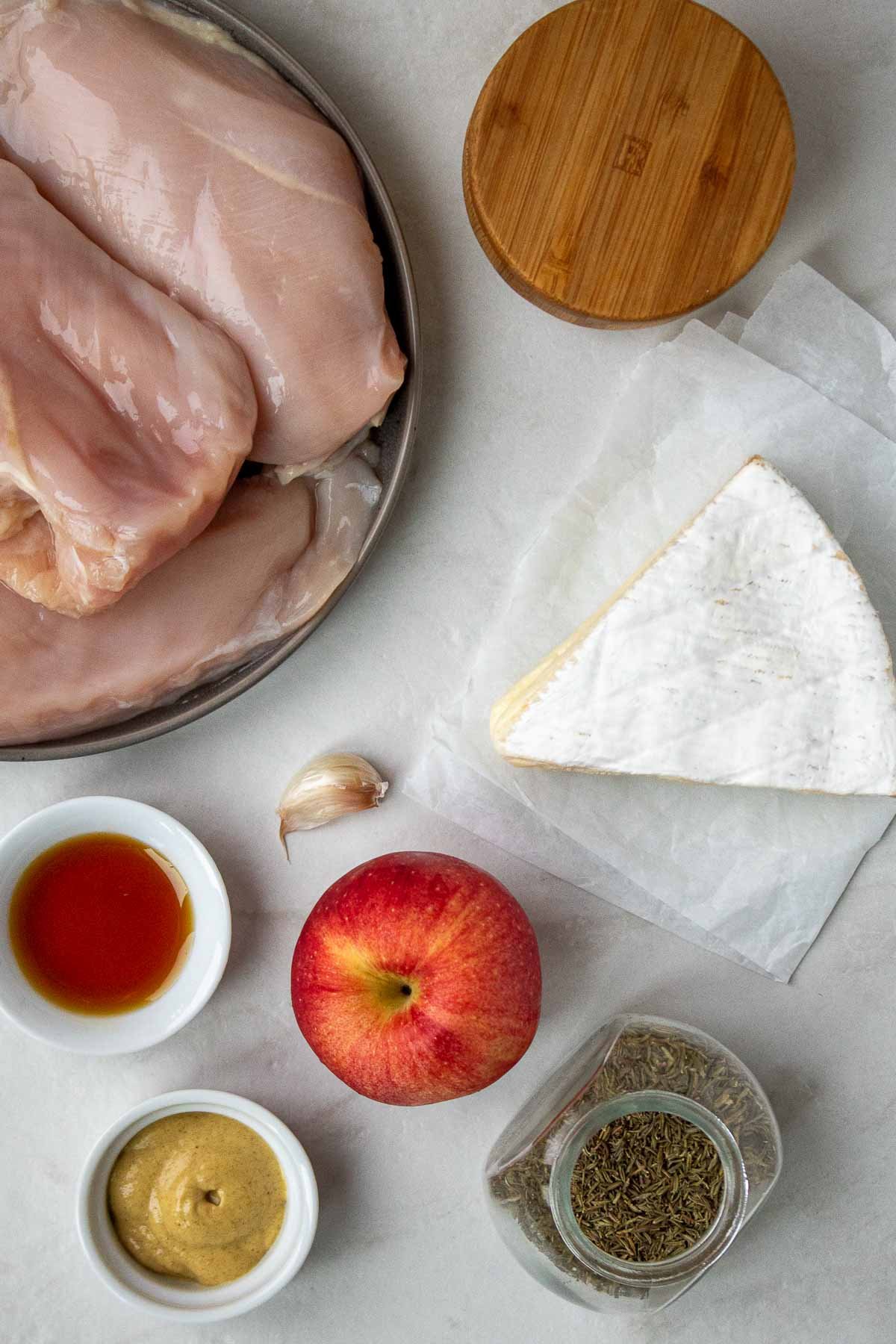 Ingredients for apple and brie stuffed chicken: chicken breasts, brie cheese, apple, Dijon mustard, dried thyme, maple syrup, garlic clove, and salt.