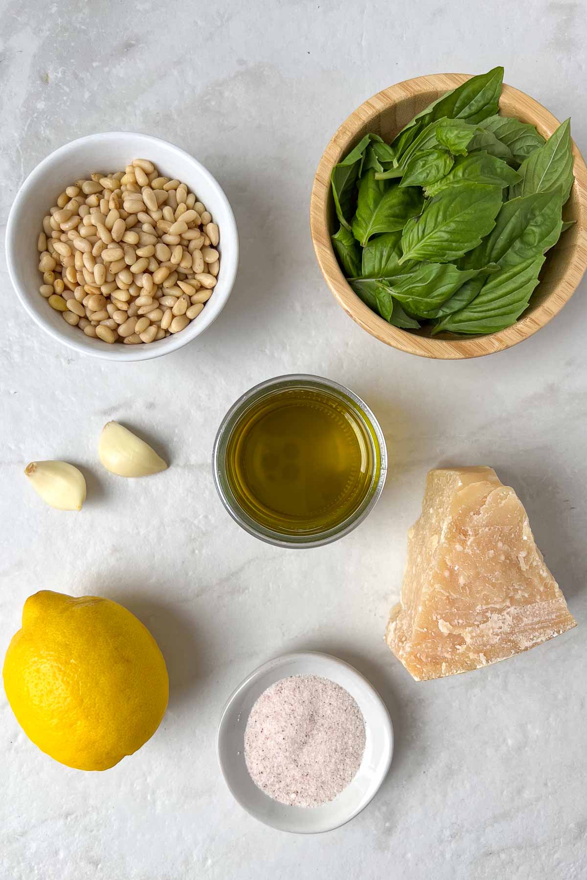 Ingredients for a homemade basil pesto recipe: basil leaves, pine nuts, garlic, parmesan cheese, lemon juice, olive oil, salt, and pepper.