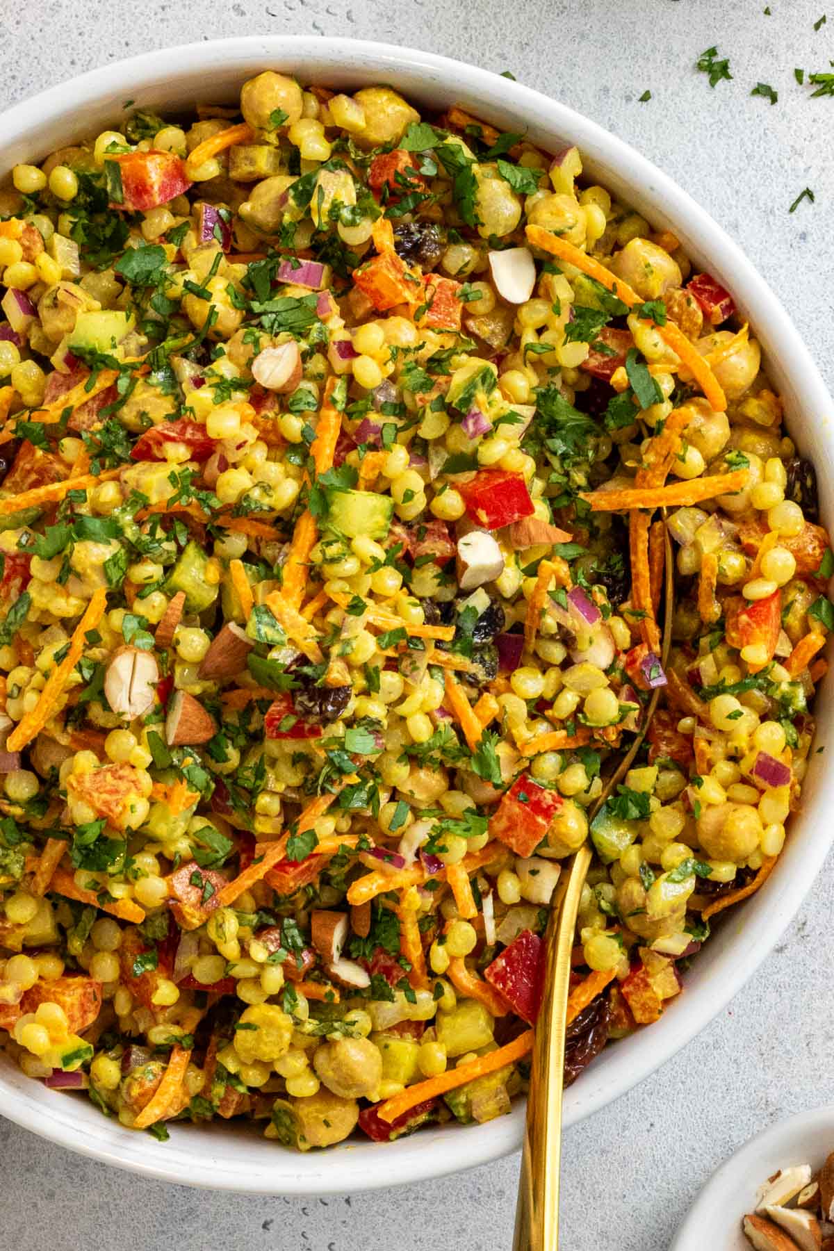 Close up of chickpea couscous salad with a serving spoon and lemon curry dressing in the background.
