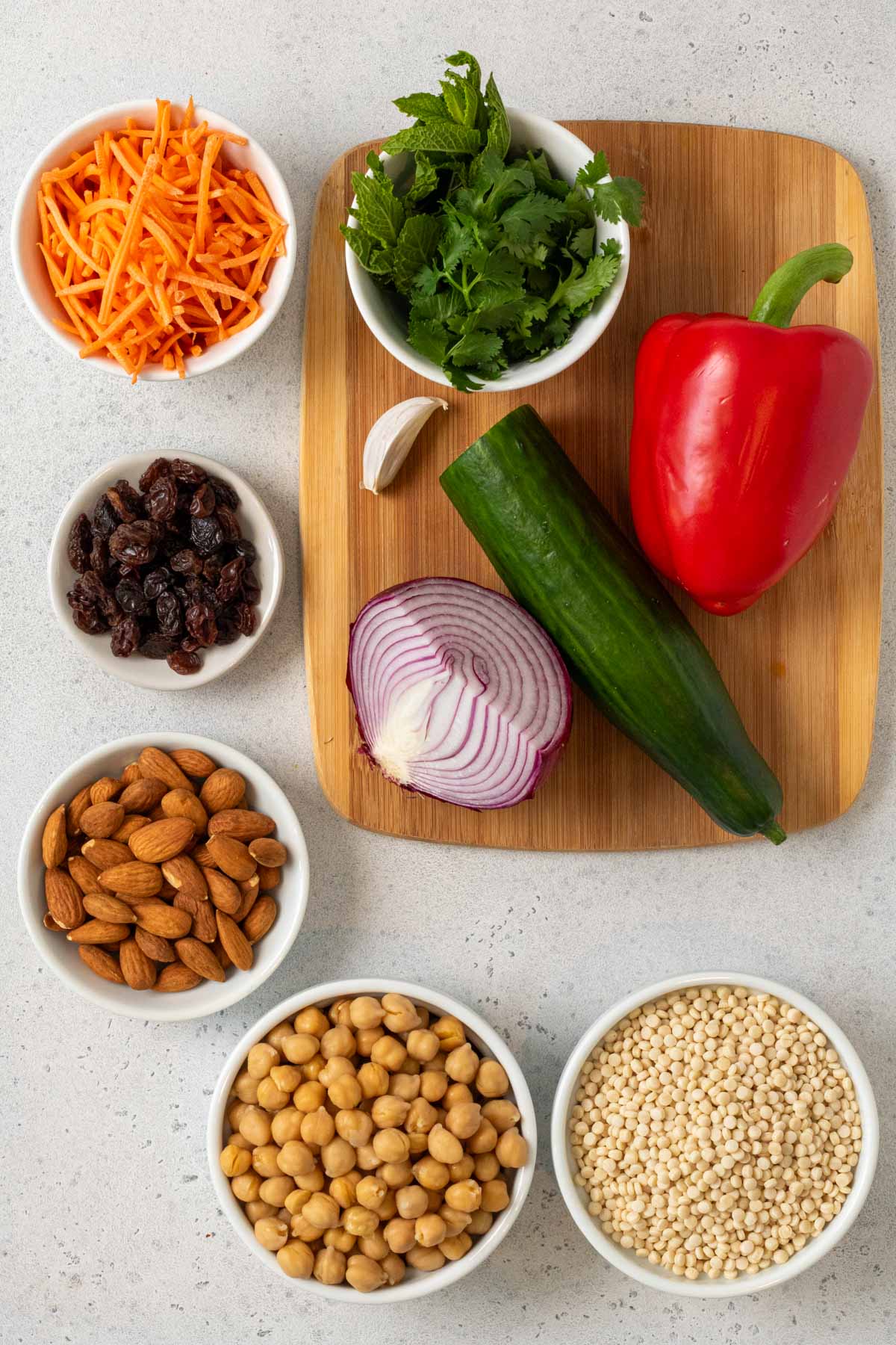 Ingredients for couscous chickpea salad; pearl couscous, red pepper, red onion, cucumber, cilantro, raisins, almonds, olive oil, mayonnaise, lemon, garlic, curry podwer, salt, and pepper.