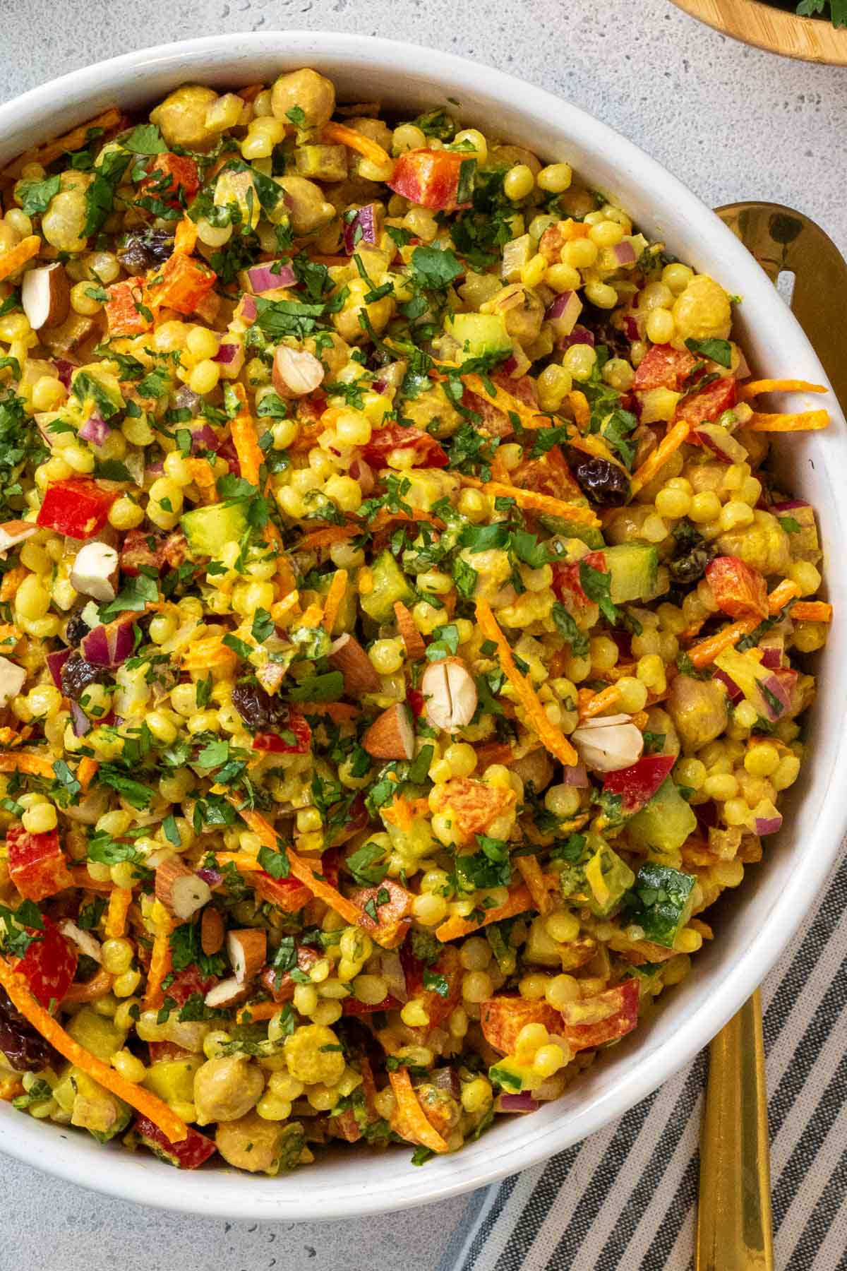Close up of a bowl curry couscous chickpea salad in a white bowl with a serving spoon and a tea towel.