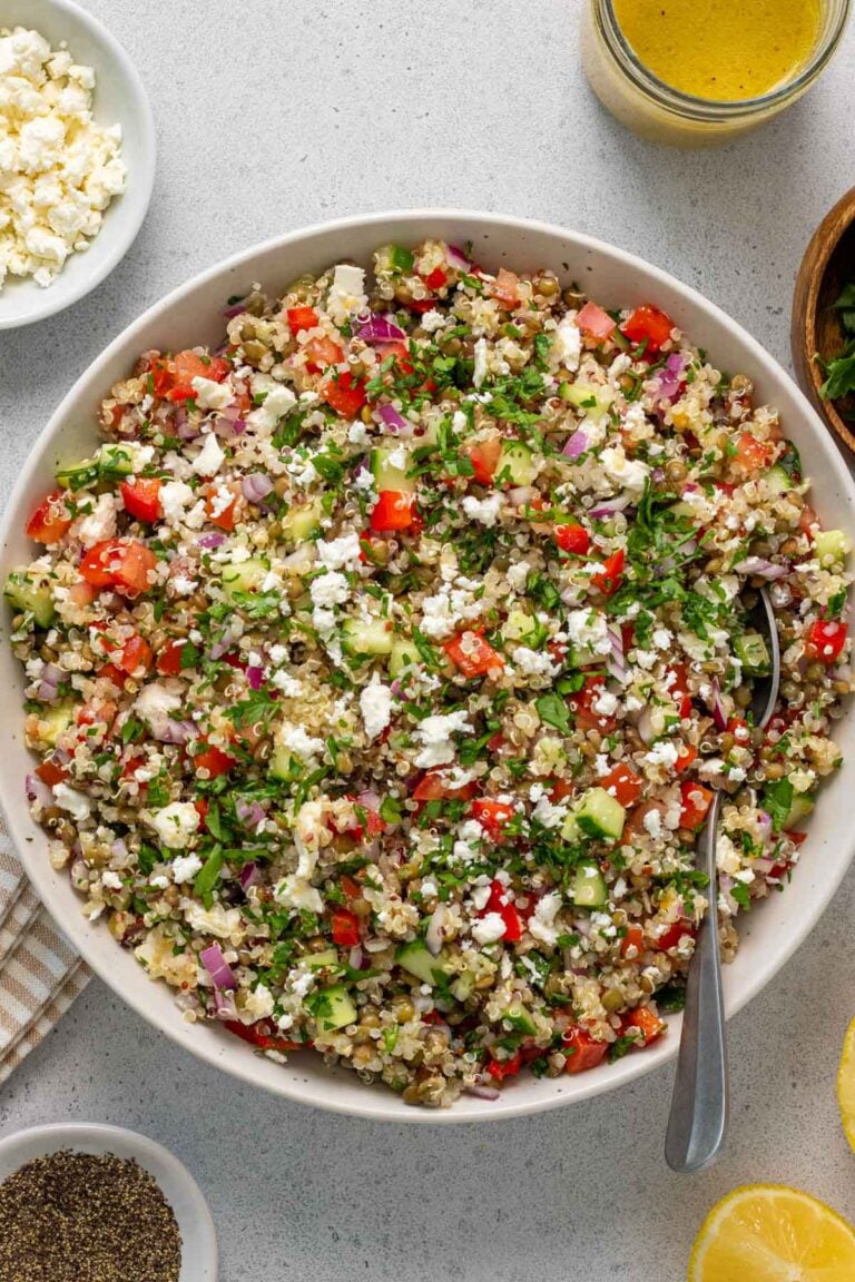 Lentil and quinoa salad in a white bowl with a serving spoon with a side of lemon dressing.