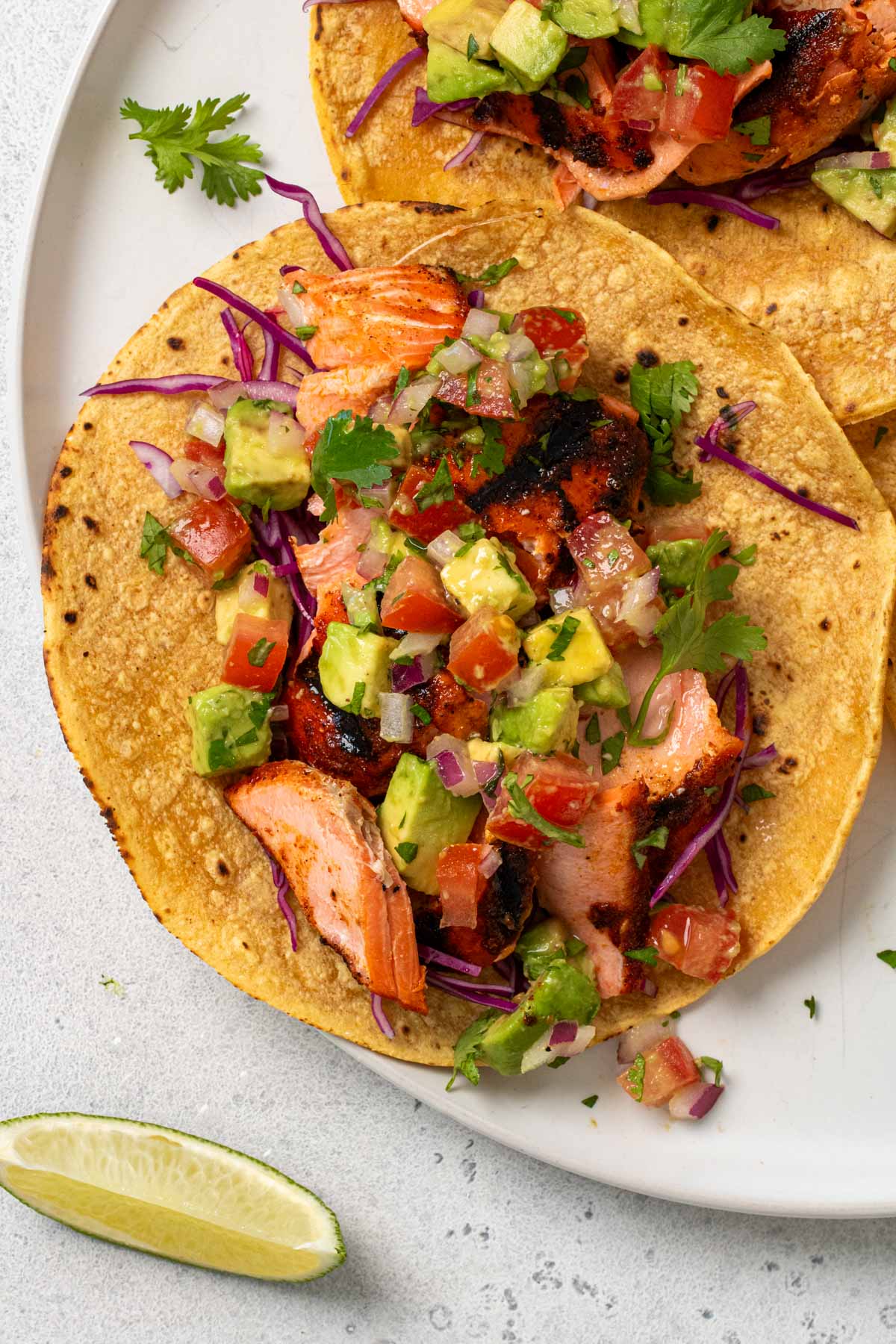 Close up of grilled salmon tacos with avocado salsa and fresh cilantor on tops.
