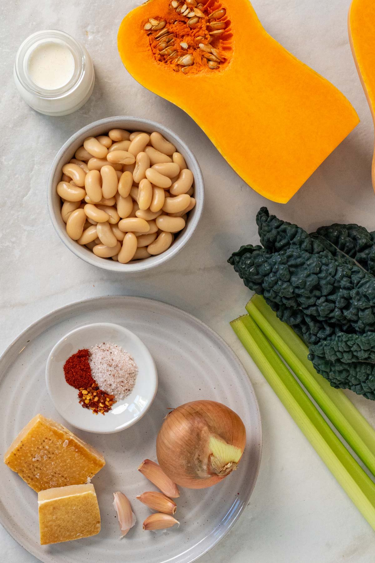 Ingredients for white bean, kale, and butternut squash soup: cubed butternut squash, cannelini beans, lacinato kale, onion, garlic, celery, paprika, chili flakes, salt, parmesan rind, broth, and heavy cream.