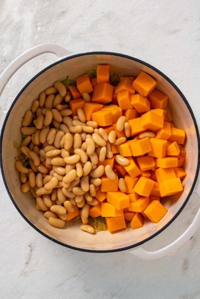 Large pot with sautéed onions, spices, butternut squash, and white beans.