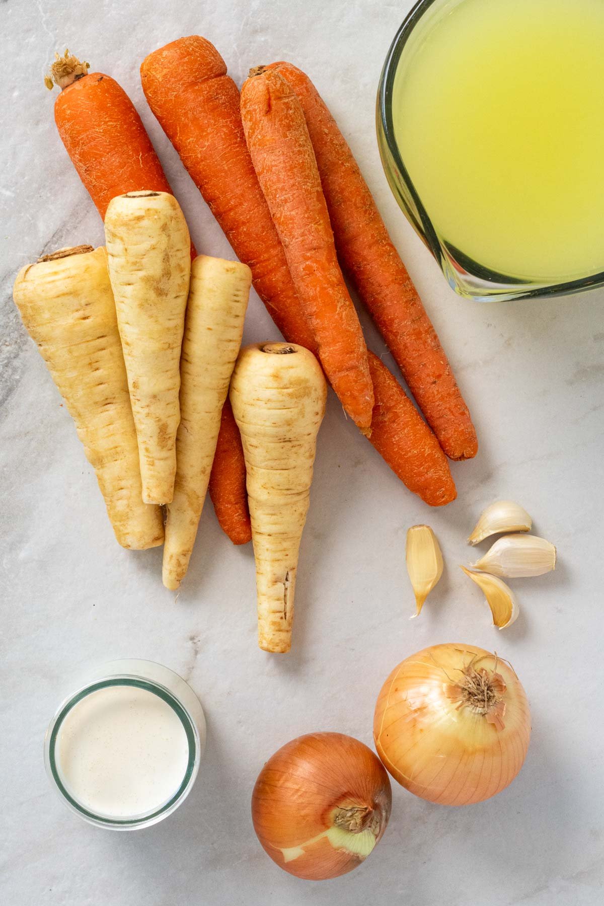 Ingredients for carrot and parsnip soup; carrots, parsnips, onions, garlic, broth, cream, salt, and pepper.