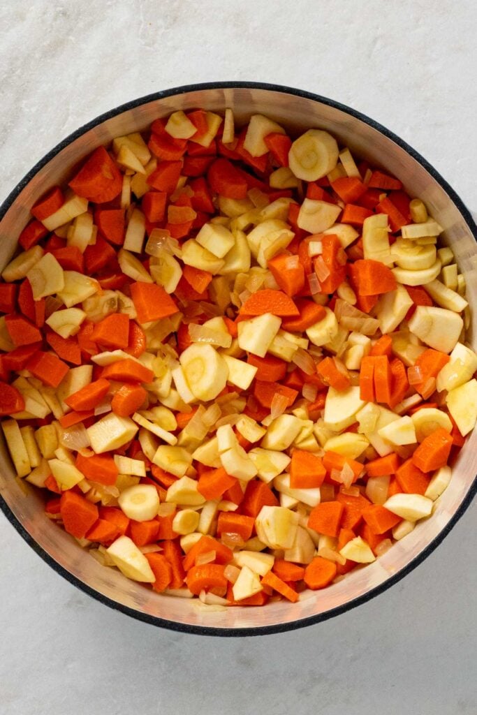 Dutch oven with sautéed onion, chopped carrots, chopped parsnips, and garlic.