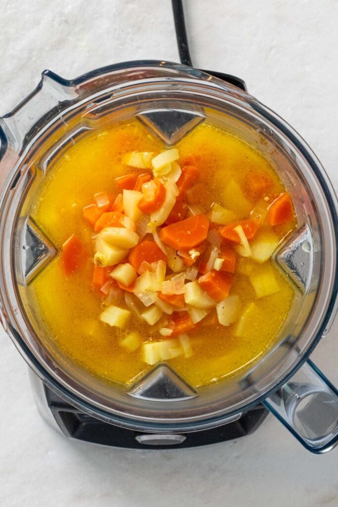 Blender with cooked carrots and parsnips in broth.