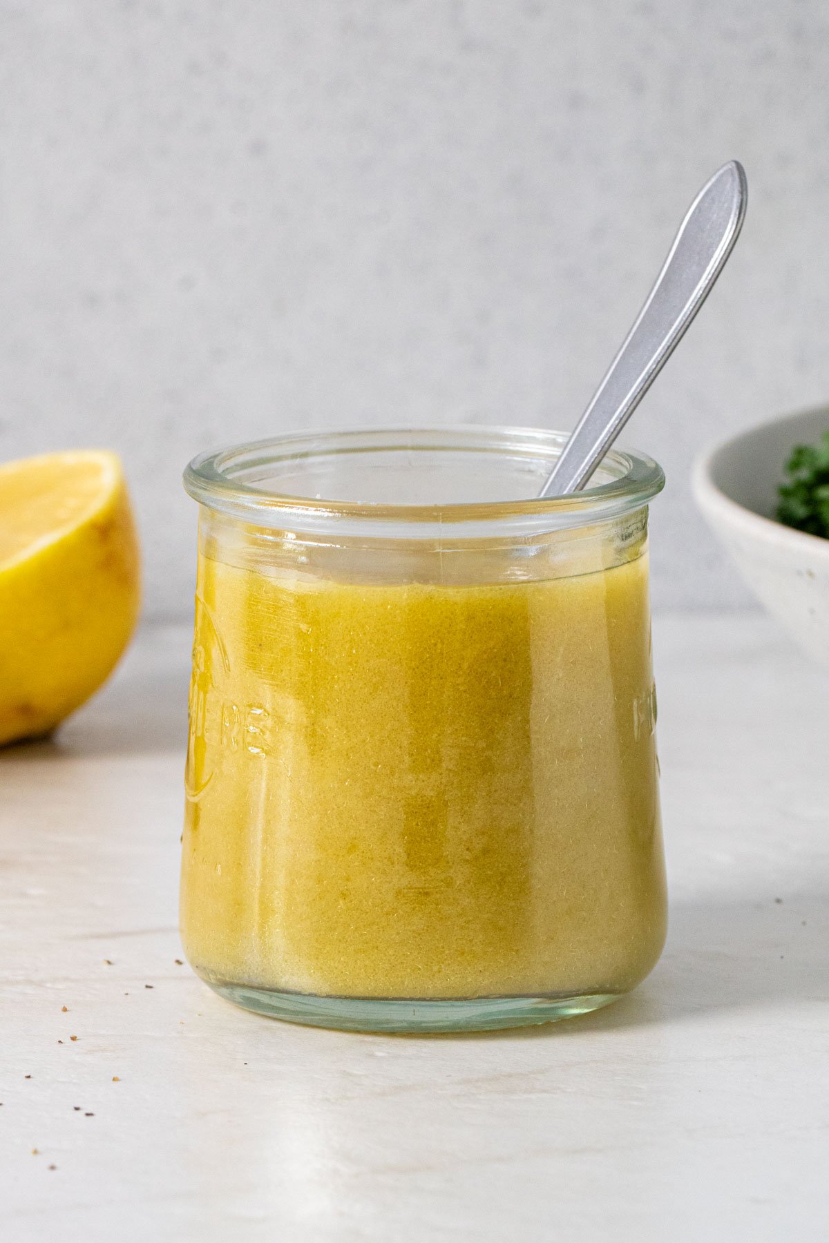 Jar of lemon vinaigrette with half a lemon and a bowl of kale in the background.