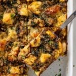 White baking dish with egg, sausage, and bread casserole with a slice on a spatula.
