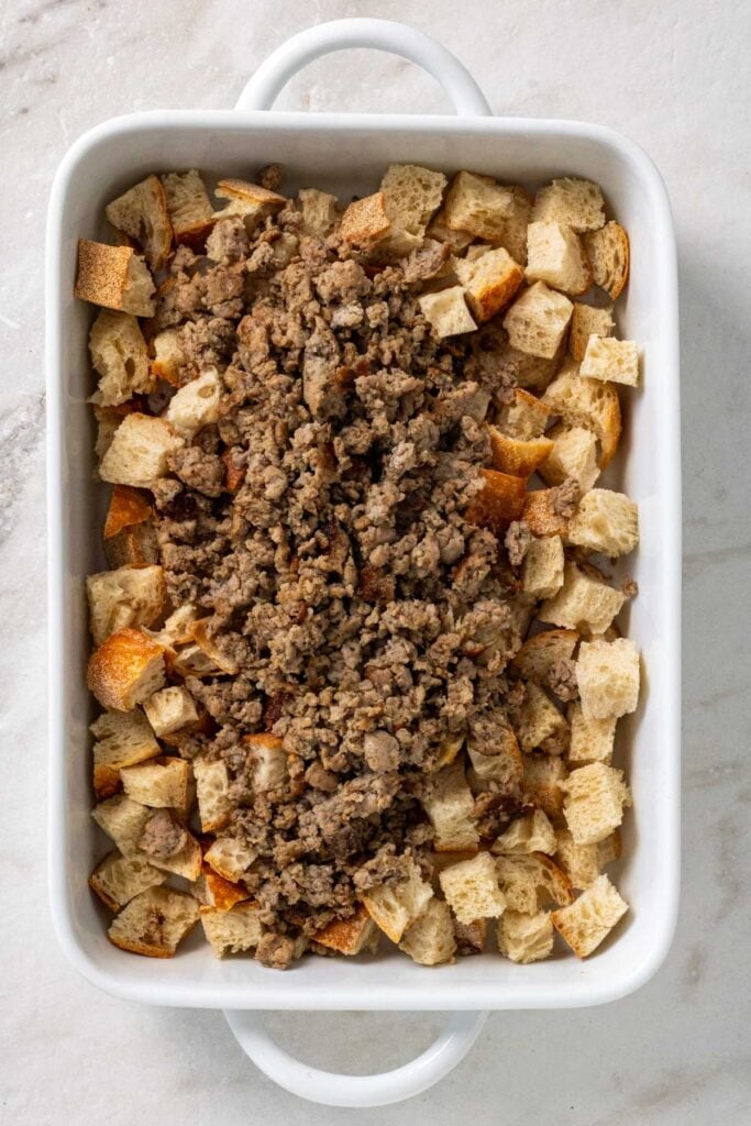 Baking dish with bread cubes and cooked pork sausage.