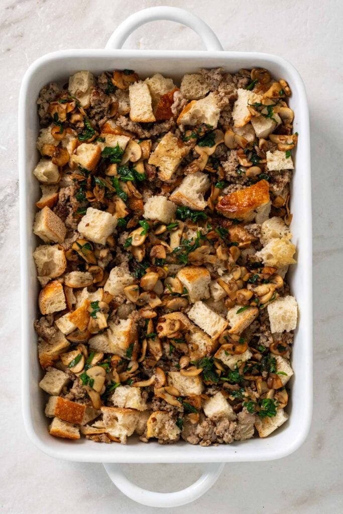 Baking dish with bread cubes, pork sausage, sautéed onion, garlic, spinach, and mushrooms. 