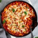 Ground turkey pasta bake in a cast-iron skillet with fresh basil on top, a serving spoon, and a side of crushed red pepper flakes.